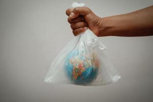 mano che tiene il globo in un sacchetto di plastica su sfondo grigio concetto giorno della terra foto