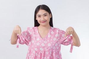 la bella donna asiatica con i capelli lunghi neri in camicia rosa mostra la mano puntata verso il basso per presentare qualcosa su sfondo bianco. foto