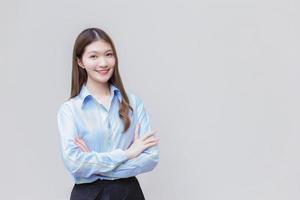 la donna asiatica che lavora con i capelli lunghi indossa una camicia blu mentre incrocia il braccio e sorride felicemente su sfondo bianco. foto