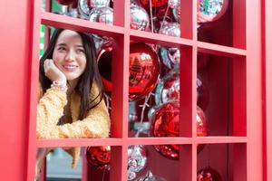 bella donna asiatica dai capelli lunghi che indossa una veste gialla e un sorriso felice in piedi nella cabina telefonica rossa nel tema della celebrazione del natale e del felice anno nuovo foto