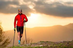 atleta uomo che pratica il sentiero con i bastoni al tramonto foto