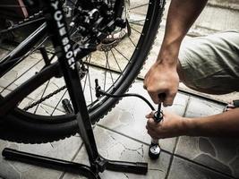 le mani di un uomo che pompano un pneumatico da bicicletta usando una piccola pompa. foto