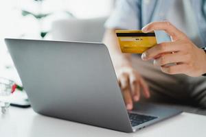 mano che tiene la carta di credito e utilizza il laptop. uomo d'affari o imprenditore che lavora da casa. shopping online, e-commerce, internet banking, spesa di denaro, concetto di lavoro da casa foto