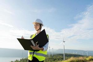 giovane donna ingegnere che lavora con il rapporto negli appunti contro la fattoria di turbine eoliche foto