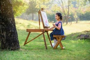 una bambina è seduta sulla panca di legno e dipinta sulla tela posta su un leggio da disegno foto