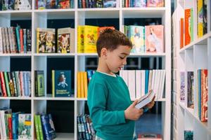 un ragazzino cerca uno scaffale di libri per bambini in libreria. foto