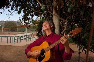 uomo maturo felice che canta e suona la sua chitarra acustica nel parco foto