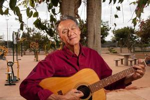 uomo maturo felice che canta e suona la sua chitarra acustica nel parco foto