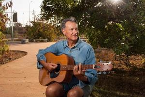 uomo maturo felice che canta e suona la sua chitarra acustica nel parco foto