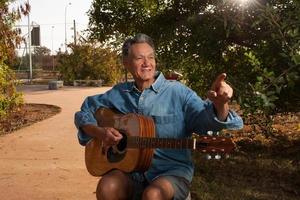 uomo maturo felice che canta e suona la sua chitarra acustica nel parco foto