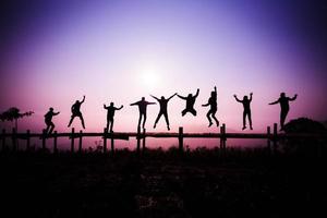 silhouette saltando gli amici della squadra che saltano sul ponte di legno sulla collina - felice e divertente divertiti a saltare le persone con l'alba foto