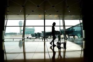 silhouette passeggero che cammina al terminal dell'aeroporto con carrello per i bagagli foto