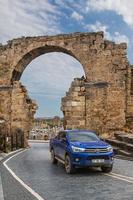 lato turchia 20 febbraio 2022 il pickup blu toyota hilux sta guidando in una calda giornata estiva sullo sfondo di un antico cancello ad arco. foto