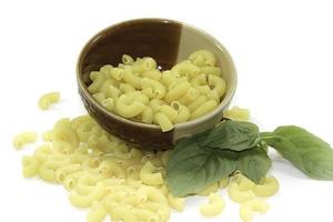 i maccheroni crudi sono un ingrediente delizioso della cucina italiana che è popolare in tutto il mondo ed è uno dei preferiti in Europa e le foglie di basilico in un piatto su uno sfondo bianco. foto