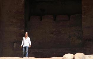 giovane uomo che indossa un cappello in un edificio monumentale scavato nella roccia nell'antica città giordana di petra. foto