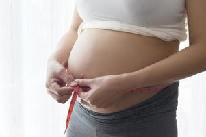 giovane donna incinta che misura il centimetro della pancia, l'assistenza sanitaria e la gravidanza foto