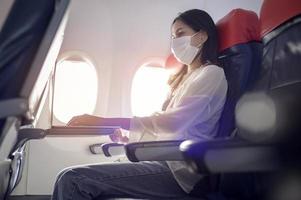 la giovane donna che indossa la maschera facciale sta utilizzando lo smartphone a bordo, un nuovo viaggio normale dopo il concetto di pandemia covid-19 foto