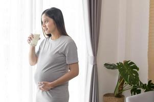 giovane donna incinta che beve latte a casa, assistenza sanitaria e gravidanza foto