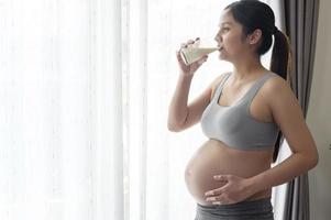 giovane donna incinta che beve latte a casa, assistenza sanitaria e gravidanza foto