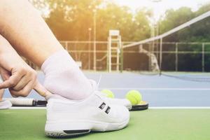 il tennista sta mettendo la scarpa prima della partita nel campo da tennis in cemento foto