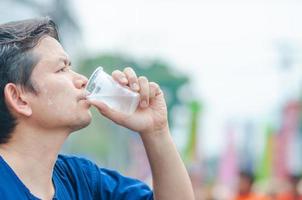 l'uomo tailandese settentrionale beve acqua fresca e fredda in un bicchiere di plastica durante la partecipazione all'attività all'aperto in una giornata molto calda indossando una camicia in stile tailandese settentrionale foto