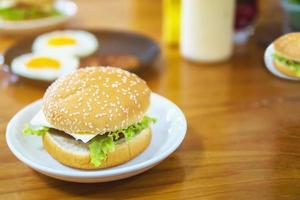 colazione a base di hamburger con uova fritte sfocate e sfondo di condimento sul tavolo di legno - delizioso concetto di colazione fast food foto