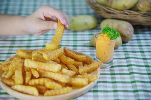 mano che tiene una deliziosa patata fritta su un piatto di legno con salsa tuffata - concetto tradizionale di fast food foto