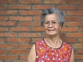 una donna asiatica anziana in piedi e guardando la fotocamera con sfondo muro di mattoni foto