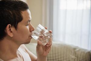 l'uomo asiatico beve acqua dopo essersi svegliato la mattina seduto su un letto - concetto di assistenza sanitaria foto