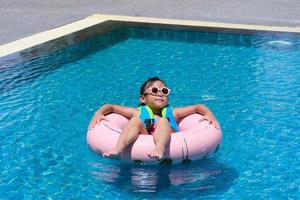 bambina in costume da bagno rilassante sull'anello gonfiabile in piscina. bambina carina che gioca in piscina in una giornata di sole. concetto di stile di vita estivo. foto