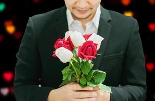 uomo che dà rose bouquet rosse e bianche a qualcuno nel giorno di San Valentino o in un altro evento del festival dell'amore con sfondo bokeh cuore colorato nero e sfocato foto