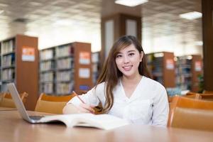 bella studentessa asiatica che utilizza computer portatile per lo studio nella biblioteca foto
