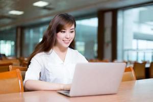 bella studentessa asiatica che utilizza computer portatile per lo studio nella biblioteca foto
