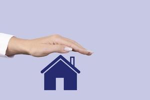 concetto di vendita, affitto, assicurazione e protezione immobiliare. una mano femminile copre l'icona con una casa. copia spazio. foto