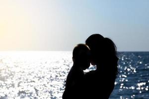 una giovane ragazza tiene in braccio un bambino contro il sole. fotografia di silhouette. foto