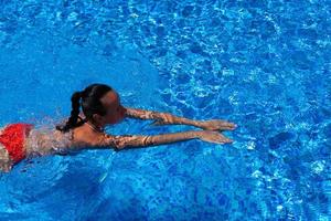 vista dall'alto di una ragazza abbronzata, femmina, modella in costume da bagno rosso, che nuota nell'acqua blu della piscina. foto