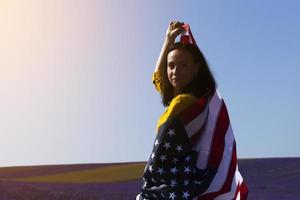 una giovane donna dai capelli scuri che tiene la bandiera degli stati uniti d'america contro il cielo soleggiato. giorno della memoria e concetto di festa dell'indipendenza degli Stati Uniti. foto