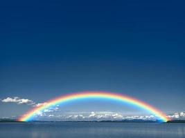 arcobaleno sul cielo blu scuro e nuvola bianca sul lago e sulla linea dell'albero e sulla piccola montagna foto