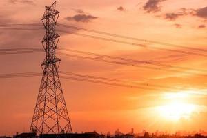 traliccio elettrico ad alta tensione e linee di trasmissione con cielo al tramonto e paesaggio urbano. tralicci elettrici. torre di rete ad alta tensione. palo di alta tensione per la distribuzione di energia elettrica alle comunità urbane. foto