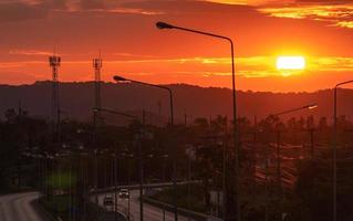 bellissima alba sulla montagna al mattino. grande sole sorge al mattino tra nuvole arancioni e rosse. le persone che guidano l'auto su una strada asfaltata curva al mattino vanno al lavoro. cielo dorato e nuvole rosse. foto