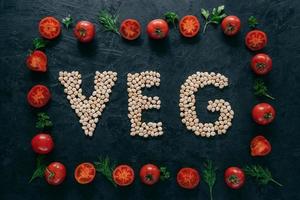 foto di cornice di pomodori e lettere di ceci che significano veg. semi organici all'interno del telaio vegetale isolato su sfondo scuro. vegetarianismo