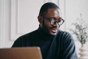 l'uomo afroamericano pensieroso si siede alla scrivania a casa, guarda la lezione di video online o il webinar sul computer foto