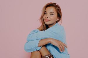 donna con un sorriso affascinante seduto isolato su sfondo rosa foto