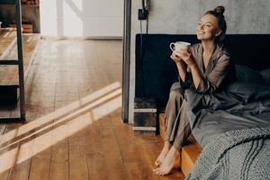 bella ragazza carina con una tazza di caffè mattutino che si rilassa mentre è seduto sul letto foto