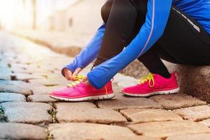 giovane donna che lega le sue scarpe da ginnastica rosa per prepararsi a una corsa foto