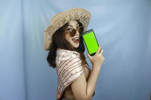 giovane donna asiatica felice che mostra lo schermo verde sul suo smartphone isolato da uno sfondo blu foto