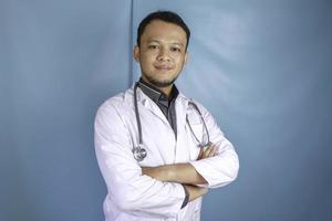 ritratto di un medico maschio attraente fiducioso, braccia sorridenti amichevoli incrociate indossare uno stetoscopio bianco da laboratorio isolato colore blu di sfondo foto