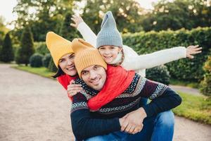 divertirsi insieme sorridente donna eccitata, uomo e la loro bambina, indossare abiti caldi a maglia, abbracciarsi, camminare nel parco, essere di buon umore. la famiglia dà sostegno, incoraggiamento foto