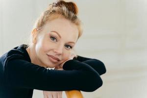 primo piano di una donna dai capelli rossi felice con il trucco, pratica il balletto in studio, si appoggia le mani sulle barre orizzontali, indossa un costume nero per la ballerina. la ballerina ha una pelle sana, si gode il riposo foto