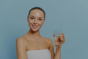 bellezza e stile di vita sano. giovane donna felice che beve acqua minerale pura, isolata sul blu foto